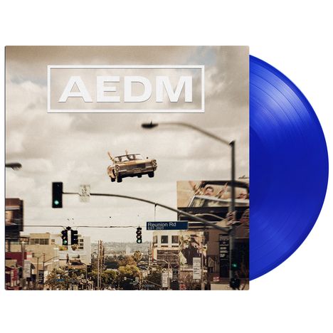 Text: "AEDM", "Reunion Rd". Auto fliegt über eine Stadtlandschaft. Blaue Schallplatte im Hintergrund.