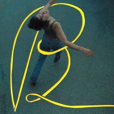 Der Buchstabe "R" in Gelb; eine Person tanzt mit ausgestreckten Armen auf Asphalt darunter.