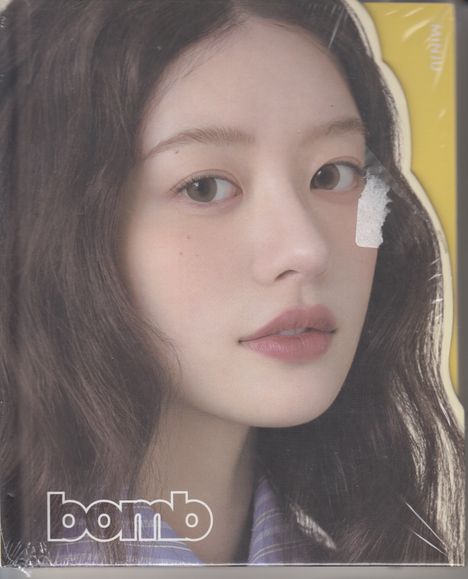 „bomb“ in weißen Buchstaben. Nahaufnahme einer Frau mit langen, dunklen Haaren vor gelbem Hintergrund. 