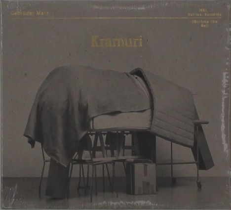 Text: „Gebrüder Marx“, „Kramuri“, „INKL Hatsune K.“
Eine Decke liegt über gestapelten Stühlen und Kisten.