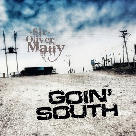"Sir Oliver Mally" und "Goin' South" stehen auf einer staubigen Straße unter bewölktem Himmel mit Stromleitungen.