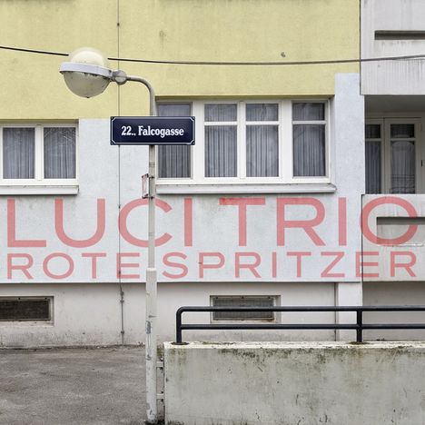 22. Falcogasse, LUCI TRIO ROTE SPRITZER. Straßenschild und Häuserfassade mit gelbem und grauem Anstrich.