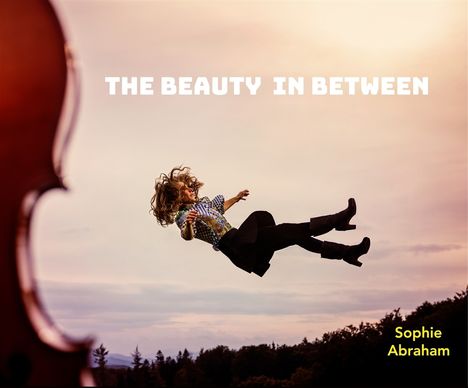 Text: "THE BEAUTY IN BETWEEN" und "Sophie Abraham". Eine Person in bunter Kleidung scheint in der Luft zu schweben, neben einem Cello.