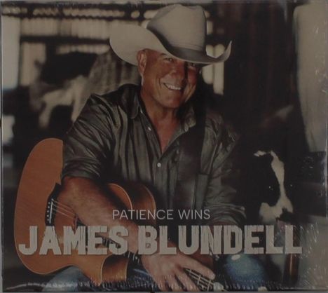 "Patience Wins, James Blundell". Ein Mann mit Cowboyhut lächelt, hält eine Gitarre und sitzt in einer rustikalen Umgebung.