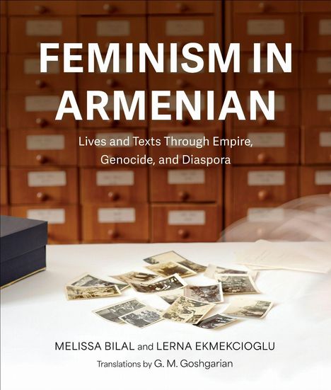 "FEMINISM IN ARMENIAN" steht in großen Buchstaben über alten Fotos auf einem Tisch. Schreibkästen im Hintergrund.