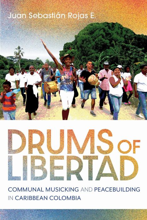 Text: "DRUMS OF LIBERTAD" – Eine Gruppe von Menschen mit Instrumenten auf einem Weg, umgeben von üppiger Vegetation.