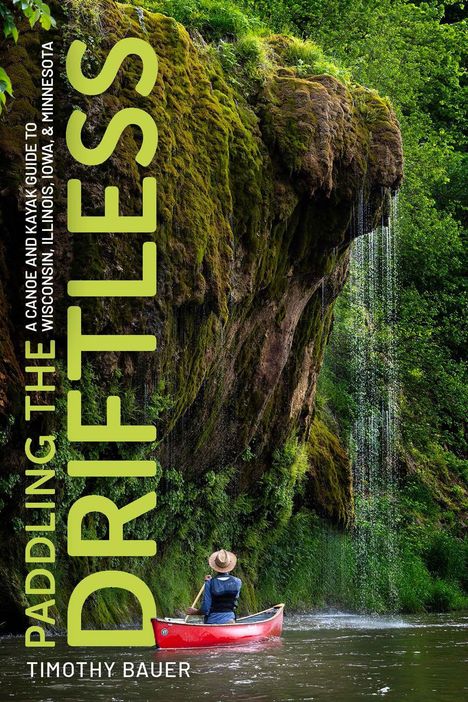 Aufschrift: Paddling the Driftless. Unter einem moosbedeckten Fels paddelt eine Person in einem roten Kanu.