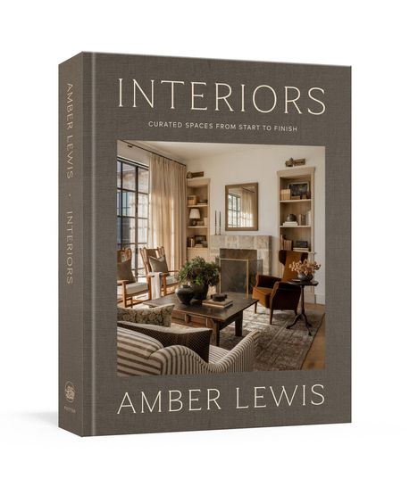 "INTERIORS" und "AMBER LEWIS" sind prominent sichtbar. Ein einladender Wohnraum mit Sofa, Kamin und Regalen.