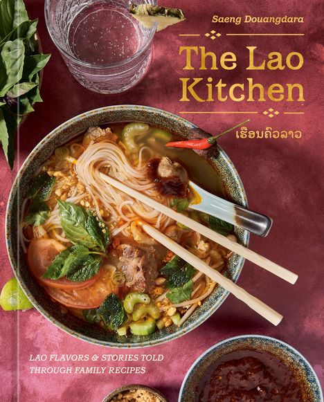 Text: "The Lao Kitchen" und "LAO FLAVORS & STORIES TOLD THROUGH FAMILY RECIPES". Nahaufnahme von Nudelsuppe und Kräutern.