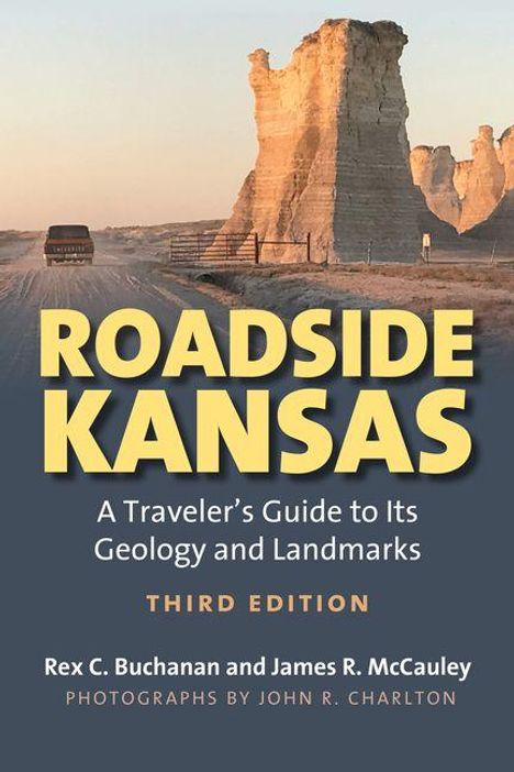 "ROADSIDE KANSAS: A Traveler’s Guide..." Ein Auto auf staubiger Straße, im Hintergrund beeindruckende Felsformationen.