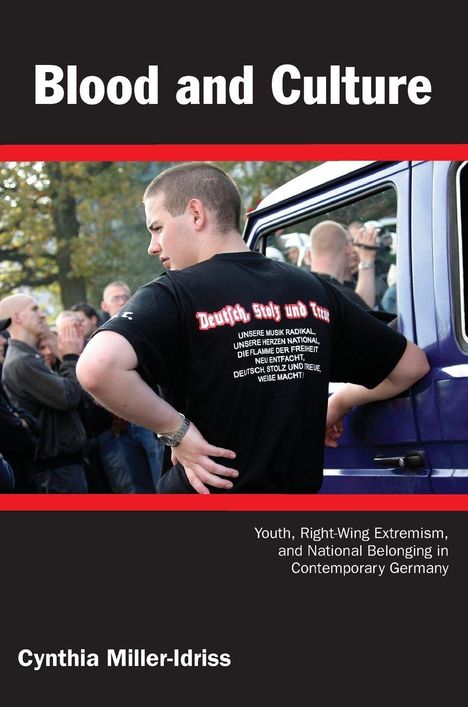 Titel: Blood and Culture. T-Shirt mit Texten über Stolz und Treue. Mann lehnt an blauem Fahrzeug. Autor: Cynthia Miller-Idriss.