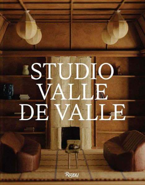 "STUDIO VALLE DE VALLE" steht im Vordergrund. Dahinter ein gemütlicher Raum mit Kamin, Regalen und Sesseln in Erdtönen.