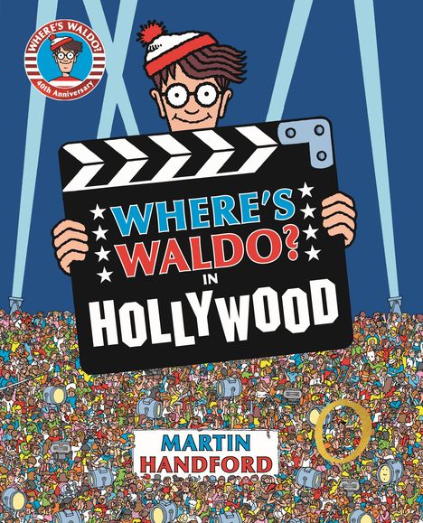 Ein Mann mit Brille und Mütze hält eine Filmklappe mit dem Text: "WHERE’S WALDO? IN HOLLYWOOD". Großer Menschenandrang.