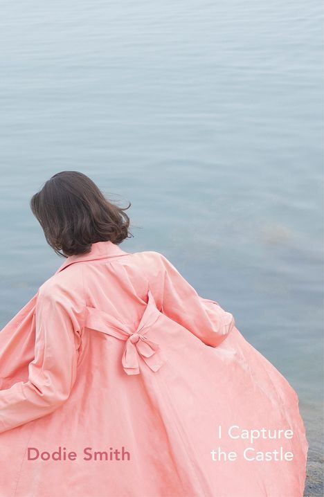 Texte: "Dodie Smith" und "I Capture the Castle". Frau im rosa Mantel vor ruhigem Wasser. Rückansicht.