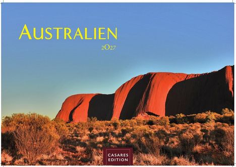 Text: "AUSTRALIEN 2027". Roter Felsen im Sonnenlicht, umgeben von niedriger Vegetation, blauer Himmel.