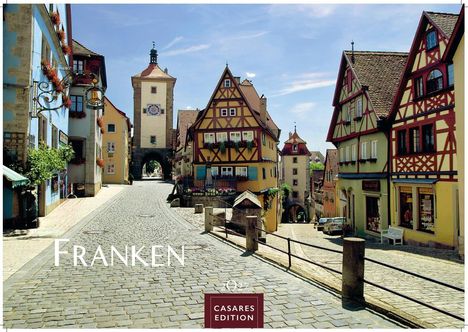 „Franken“ in großer Schrift. Kopfsteinpflasterstraße mit Fachwerkhäusern, Turm im Hintergrund, blauer Himmel.