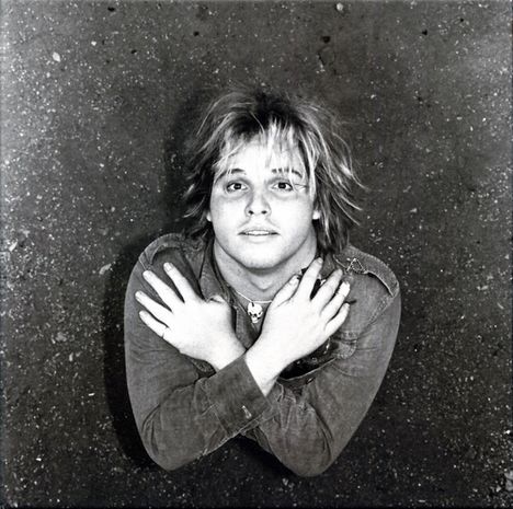 Keine Texte sichtbar. Eine Person mit langen Haaren liegt am Boden, deren Arme über der Brust gekreuzt.