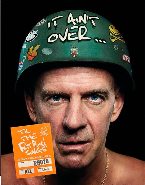 Ein Mann trägt einen Helm mit dem Text "IT AIN'T OVER..." und Aufklebern, daneben ein orangefarbenes Plakat mit weißem Text.