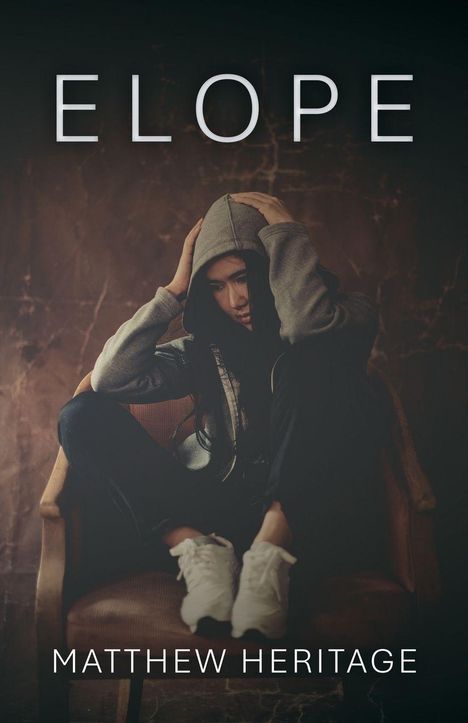 "ELOPE" und "MATTHEW HERITAGE". Eine Person in einem grauen Kapuzenpullover sitzt nachdenklich auf einem Stuhl.