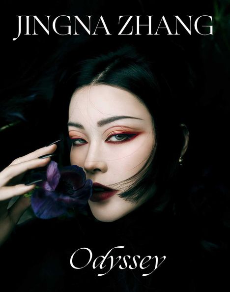 Text „JINGNA ZHANG“ oben, „Odyssey“ unten. Eine Frau mit dunklem Haar, dramatischem Augen-Make-up und einer Blume.