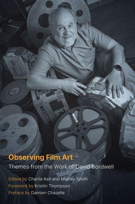 „Observing Film Art. Themes from the Work of David Bordwell. Eine Person sitzt umgeben von Filmrollen in einem Lager.“