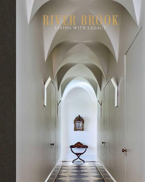 "RIVER BROOK LIVING WITH LEGACY" – Ein heller Flur mit gewölbter Decke, antikem Stuhl und verziertem Spiegel am Ende.