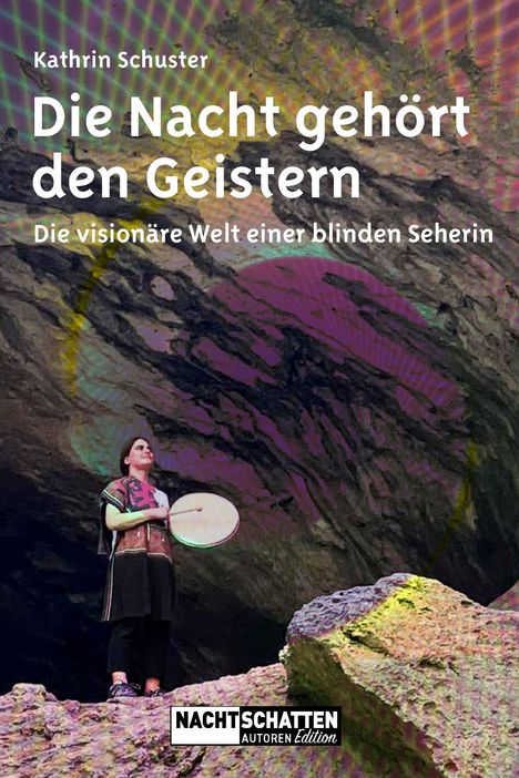 Titel: "Die Nacht gehört den Geistern" von Kathrin Schuster. Eine Frau hält eine Trommel vor einer bunten, felsigen Kulisse.