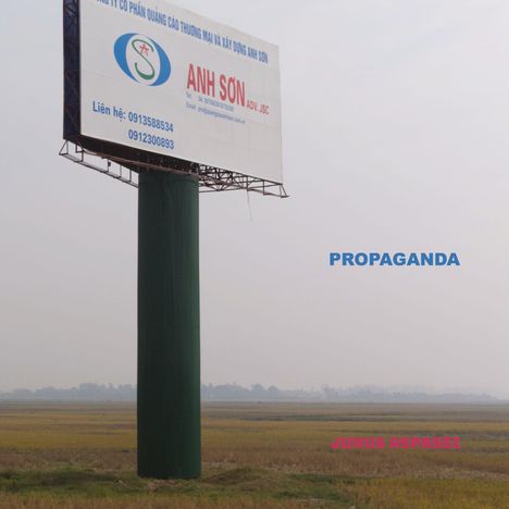 "Propaganda" in Blau, "Junus Aspassi" in Pink. Ein Werbeplakat steht auf einem Feld: Anh Son mit Kontaktdaten.