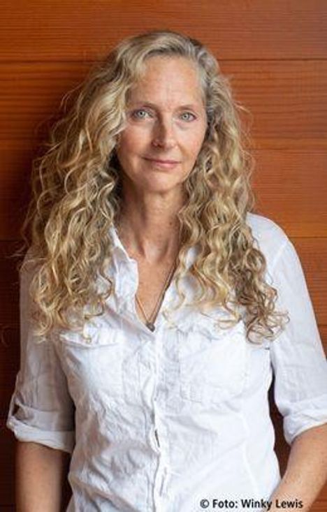 Ich kann nicht erkennen, wer auf dem Foto abgebildet ist. Es zeigt eine Person mit langen, lockigen Haaren in einem weißen Hemd.