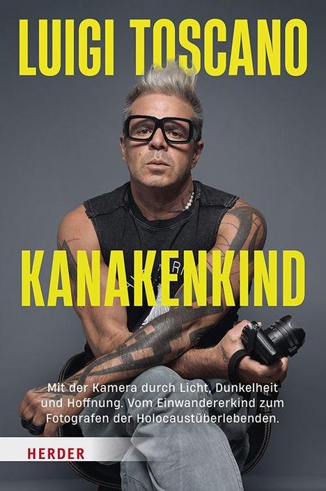 LUIGI TOSCANO, KANAKENKIND. Ein Mann mit Brille und Kamera sitzt lässig.