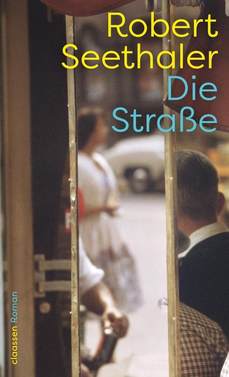 "Robert Seethaler Die Straße" in gelbe und blaue Schrift, unscharfe Straßenszene mit schemenhaften Personen im Hintergrund.