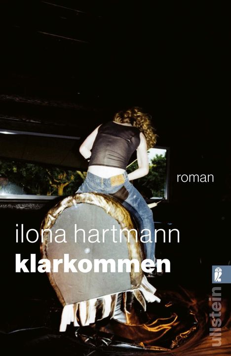 "Ilona Hartmann klarkommen roman" steht auf dem Bild. Eine Frau reitet auf einem mechanischen Bullen. Links unten ist ein Logo.