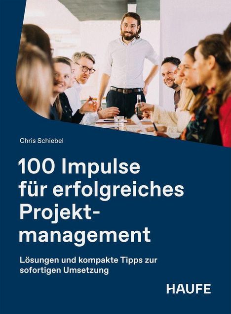 „100 Impulse für erfolgreiches Projektmanagement.“ Gruppe diskutiert am Tisch; ein Mann steht lächelnd im Hintergrund.