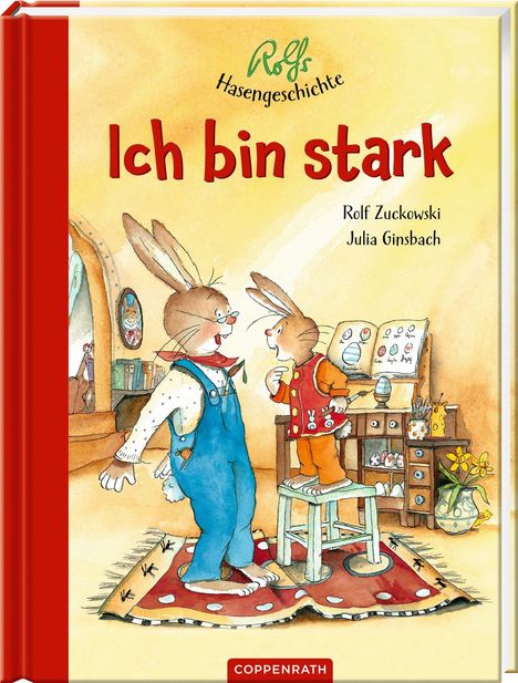„Ich bin stark“ in roter Schrift. Zwei Hasen, einer in Latzhose, der andere kleiner, stehen auf einem Hocker in einem bunten Raum.