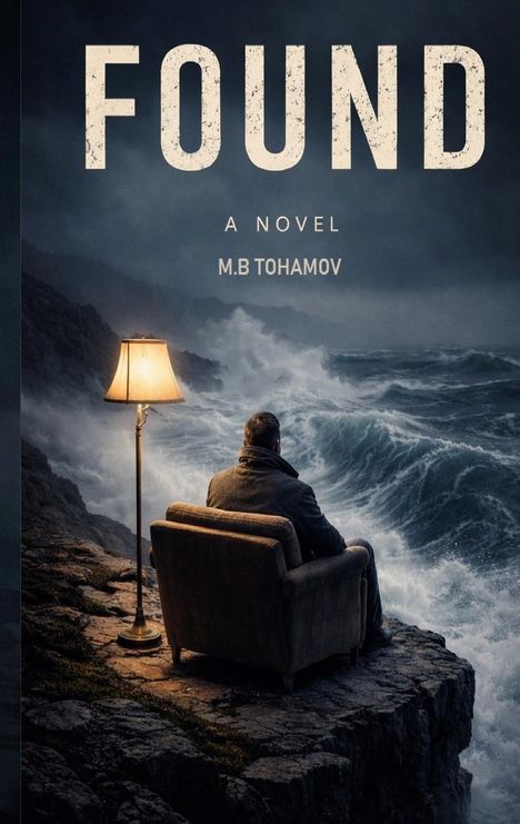 Text: "FOUND" "A NOVEL" "M.B TOHAMOV". Ein Mann sitzt auf einem Sessel am steinigen Abgrund, blickt auf stürmische See.