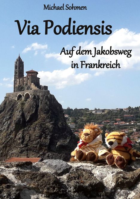 "Michael Sohmen - Via Podiensis - Auf dem Jakobsweg in Frankreich." Kirche auf Felsen, zwei Stofftiere sitzen vorne.