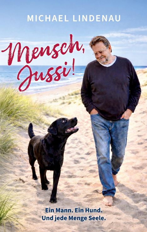 "Mensch, Jussi!" Ein Mann und ein schwarzer Hund gehen entspannt am Strand entlang.
