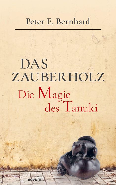 „Das Zauberholz: Die Magie des Tanuki“. Beigefarbener Hintergrund mit einer kleinen Statue eines Tieres unten rechts.