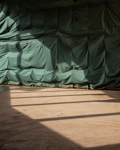 Grüne Plane, gespannt und gefaltet; Licht- und Schattenmuster auf hellem, kahlem Boden darunter.