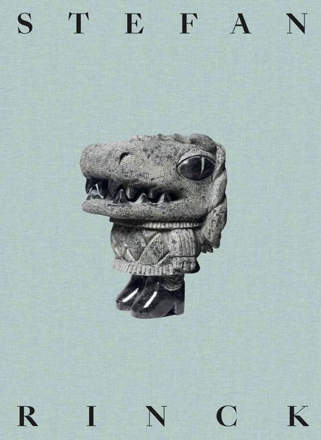 "Stefan Rinck" steht oben und unten. Eine Skulptur eines lächelnden Dinosaurierkopfs mit Pullover und Stiefeln.