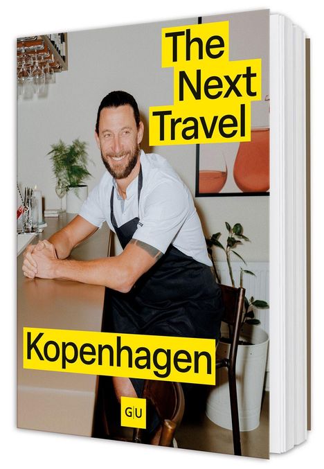 "The Next Travel. Kopenhagen." Ein Mann in einem schwarzen Schürze lächelt an einem Tresen; Pflanzen und Bilder im Hintergrund.