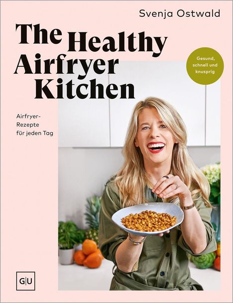 Ein Buchcover mit dem Titel "The Healthy Airfryer Kitchen" von Svenja Ostwald. Eine Frau hält einen Teller mit knusprigen, braunen Häppchen und lächelt in einer Küche.