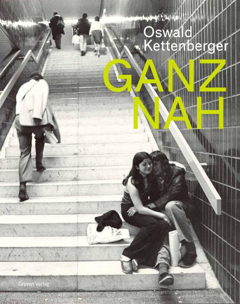 Text: "Oswald Kettenberger GANZ NAH". Zwei Menschen umarmen sich auf einer Treppe in einer U-Bahn-Station.
