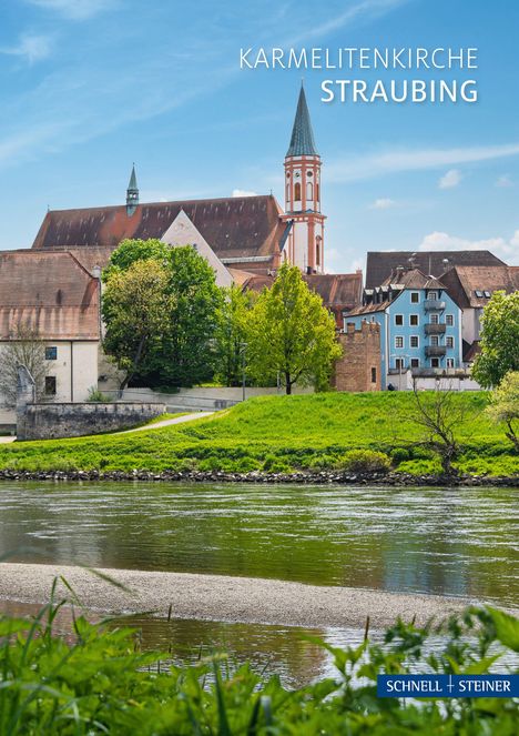 KARMELITENKIRCHE STRAUBING. Eine Kirche mit rotem Dach und Turm hinter Bäumen, am Flussufer.