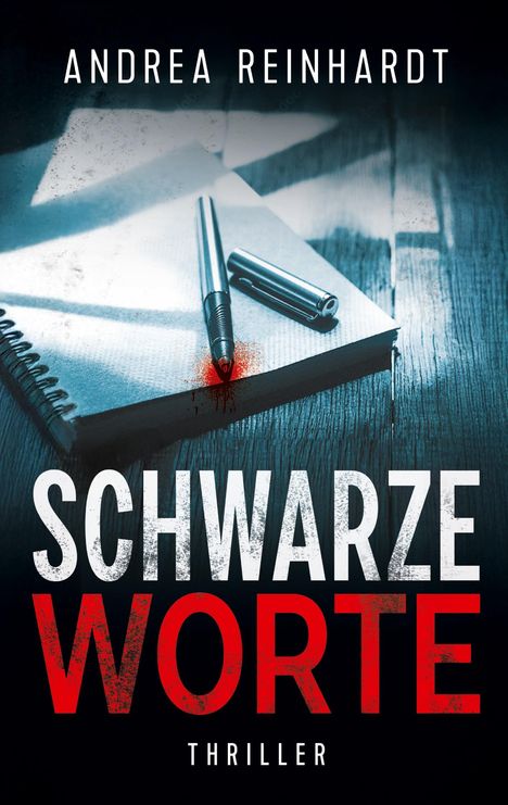 „Andrea Reinhardt. Schwarze Worte. Thriller.“ Ein Notizbuch und ein Stift mit blutrotem Fleck auf holziger Oberfläche.