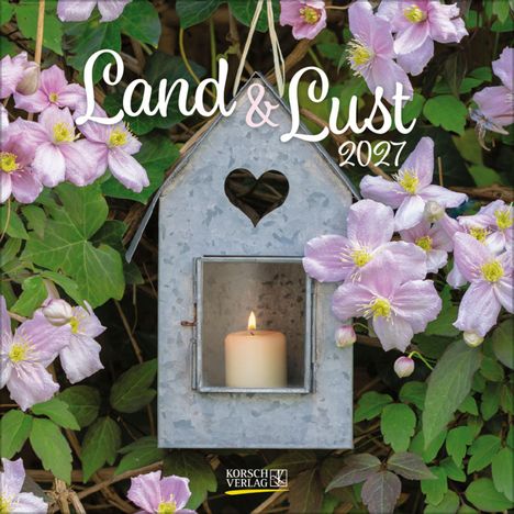 „Land & Lust 2027“. Eine Kerze brennt in einer Metalllaterne, umgeben von rosa Blüten und grünen Blättern.