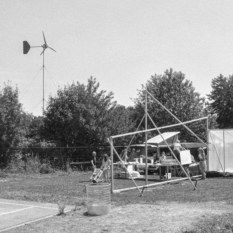Mehrere Menschen an einem Stand im Freien, umgeben von Bäumen, eine Windkraftanlage im Hintergrund.