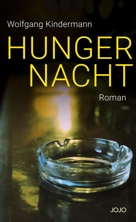 Der Text lautet: "Wolfgang Kindermann. HUNGERNACHT. Roman. JOJO." Ein Aschenbecher auf einem dunklen Tisch.
