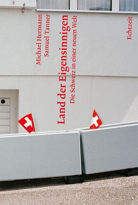 "Land der Eigensinnigen. Die Schweiz in einer neuen Welt." Zwei Schweizer Flaggen neben Betonbarrieren.