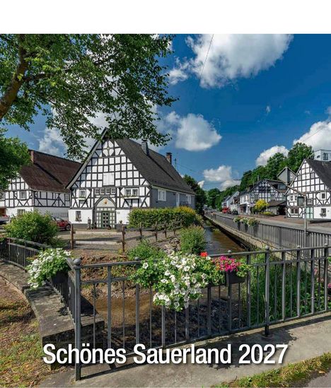 "Schönes Sauerland 2027." Fachwerkhäuser an einem kleinen, von Blumen gesäumten Bach, umgeben von grünem Laub.